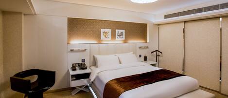 A modern hotel room with a large bed, a bedside table, a chair, and artwork on the wall.