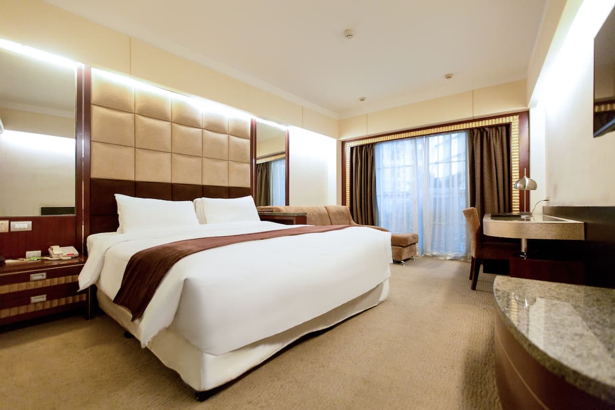 A hotel room with a large bed, a bedside table with a lamp, a chair, and a bathroom with a sink and mirror.