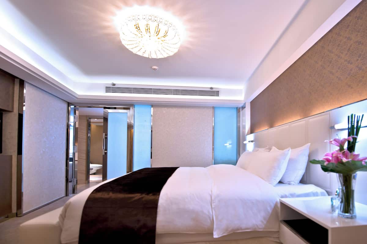 A modern hotel room with a large bed, a bedside table with a vase of flowers, and a chandelier.