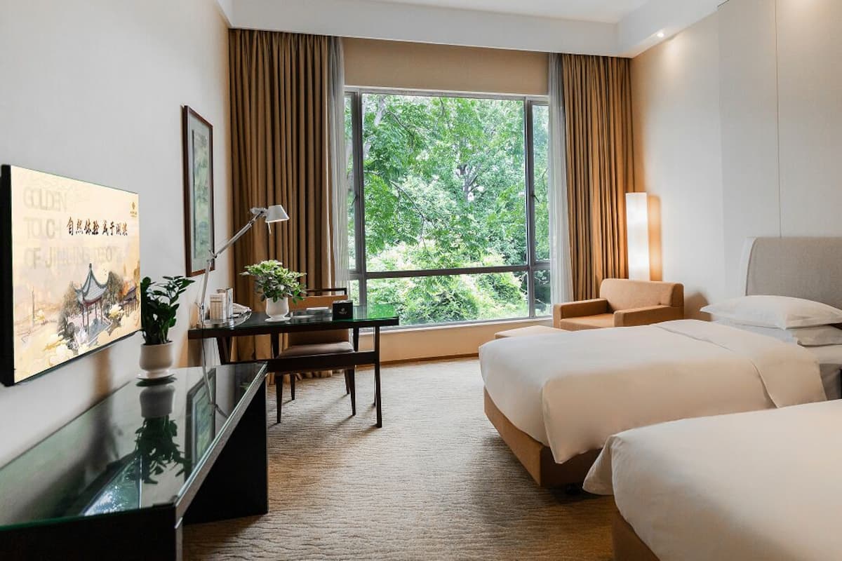 Een hotelkamer met twee bedden, een bureau, een stoel, een televisie en een groot raam met gordijnen.