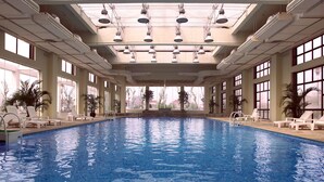An indoor swimming pool with clear blue water, surrounded by white lounge chairs and potted plants. - Jinling Resort Nanjing (Nanjing)