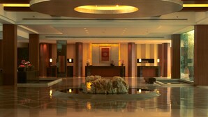 A spacious lobby with a reception desk, a large circular light fixture, and a central water feature. - Jinling Resort Nanjing (Nanjing)