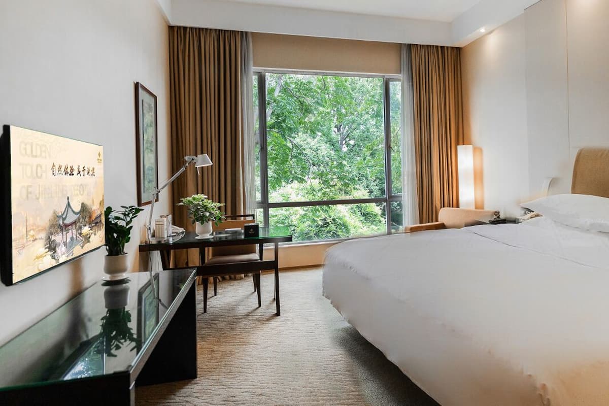 Een hotelkamer met een groot bed, een bureau met een lamp, een stoel en een raam met gordijnen.