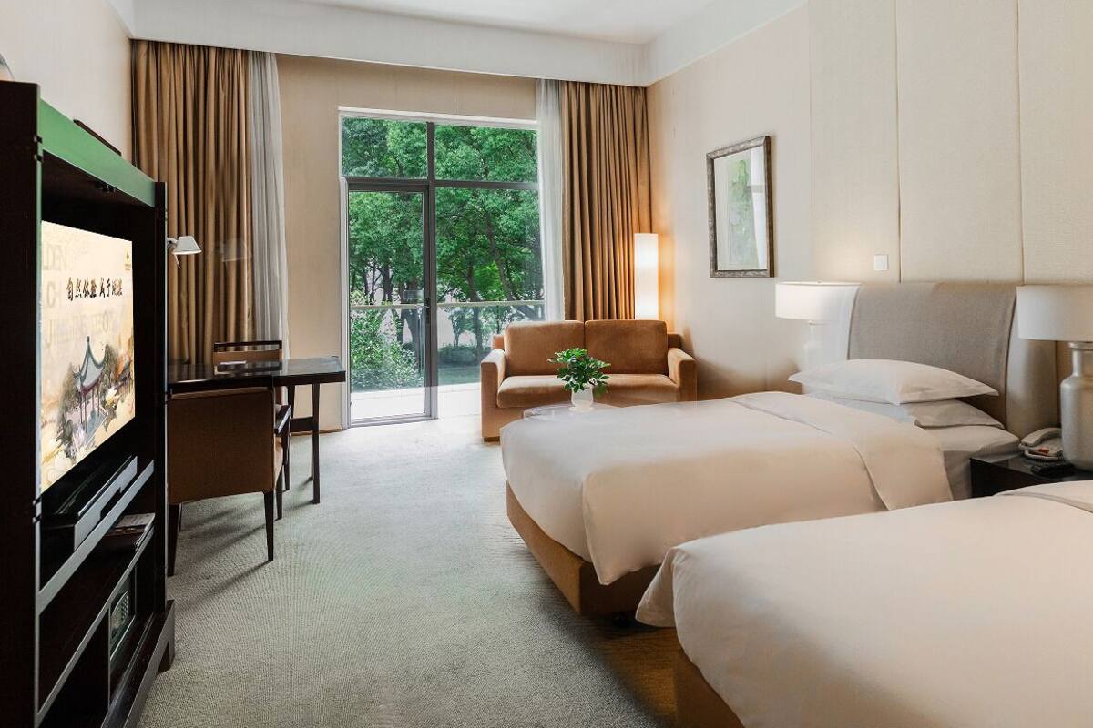 Een hotelkamer met twee bedden, een bureau, een televisie en een balkon met gordijnen.