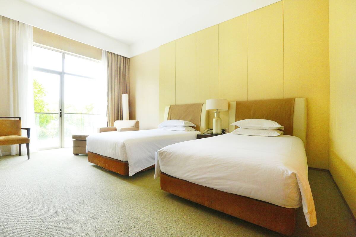 Een hotelkamer met twee bedden, een stoel, een tafeltje en uitzicht op de omgeving.