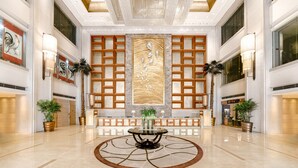 A spacious lobby with a central round table, decorative wall panels, and potted plants.