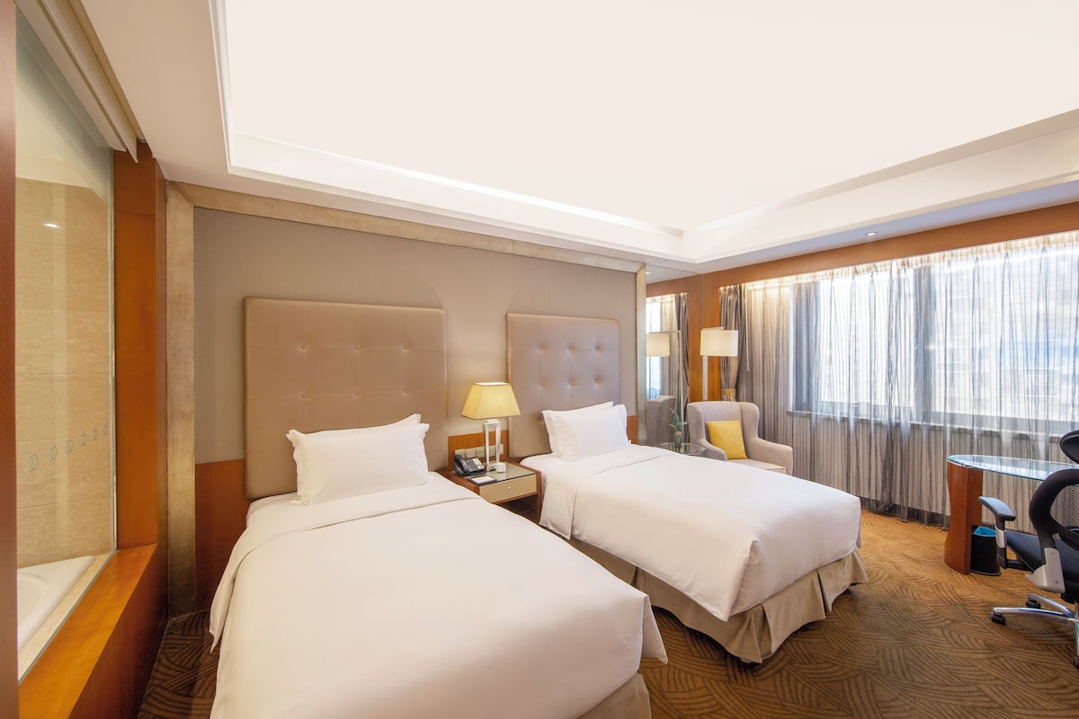 A hotel room with two beds, a desk, a chair, and a window with curtains.