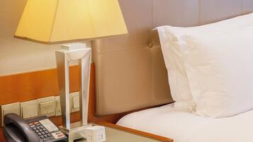 Habitación de hotel con cama, mesita de noche con lámpara, teléfono y un pequeño escritorio con bloc de notas.