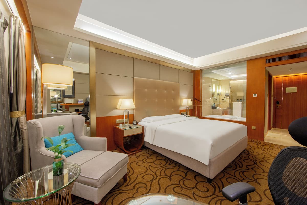 A hotel room with a bed, a sofa, a small table with a vase, and a chair.