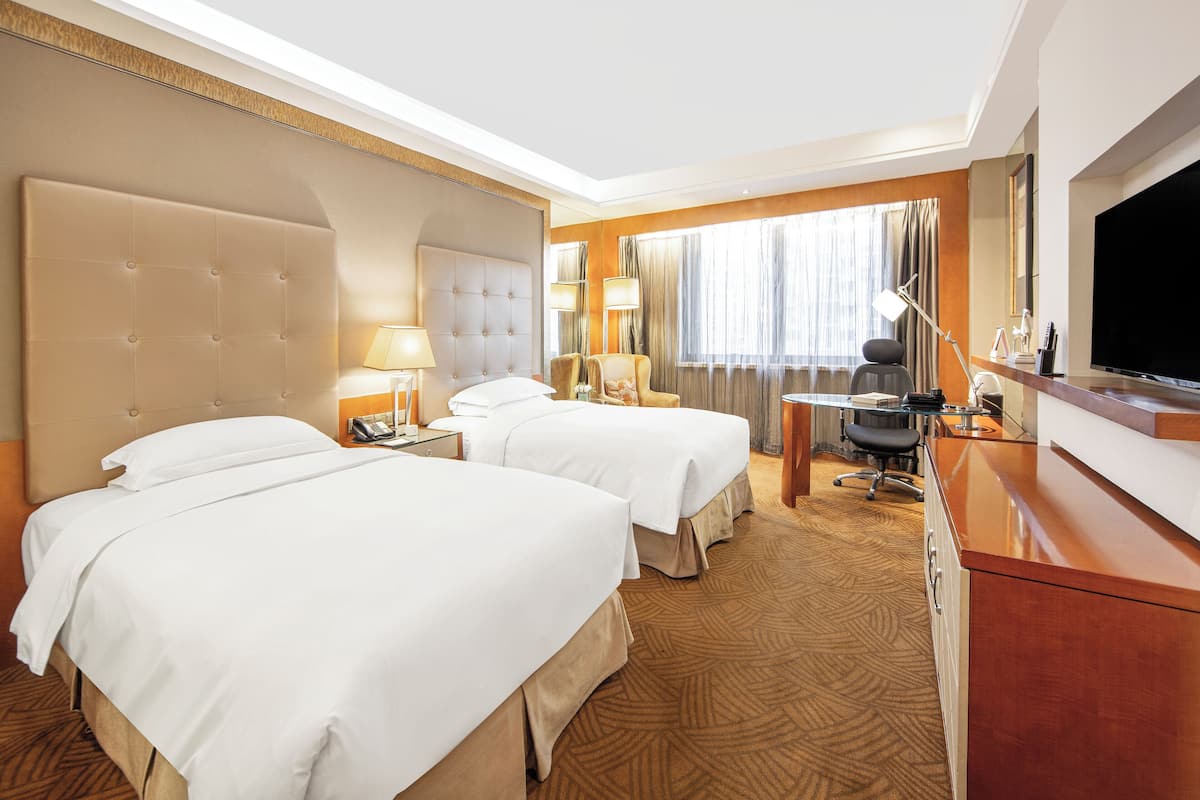 A hotel room with two beds, a desk, a TV, and a minibar.