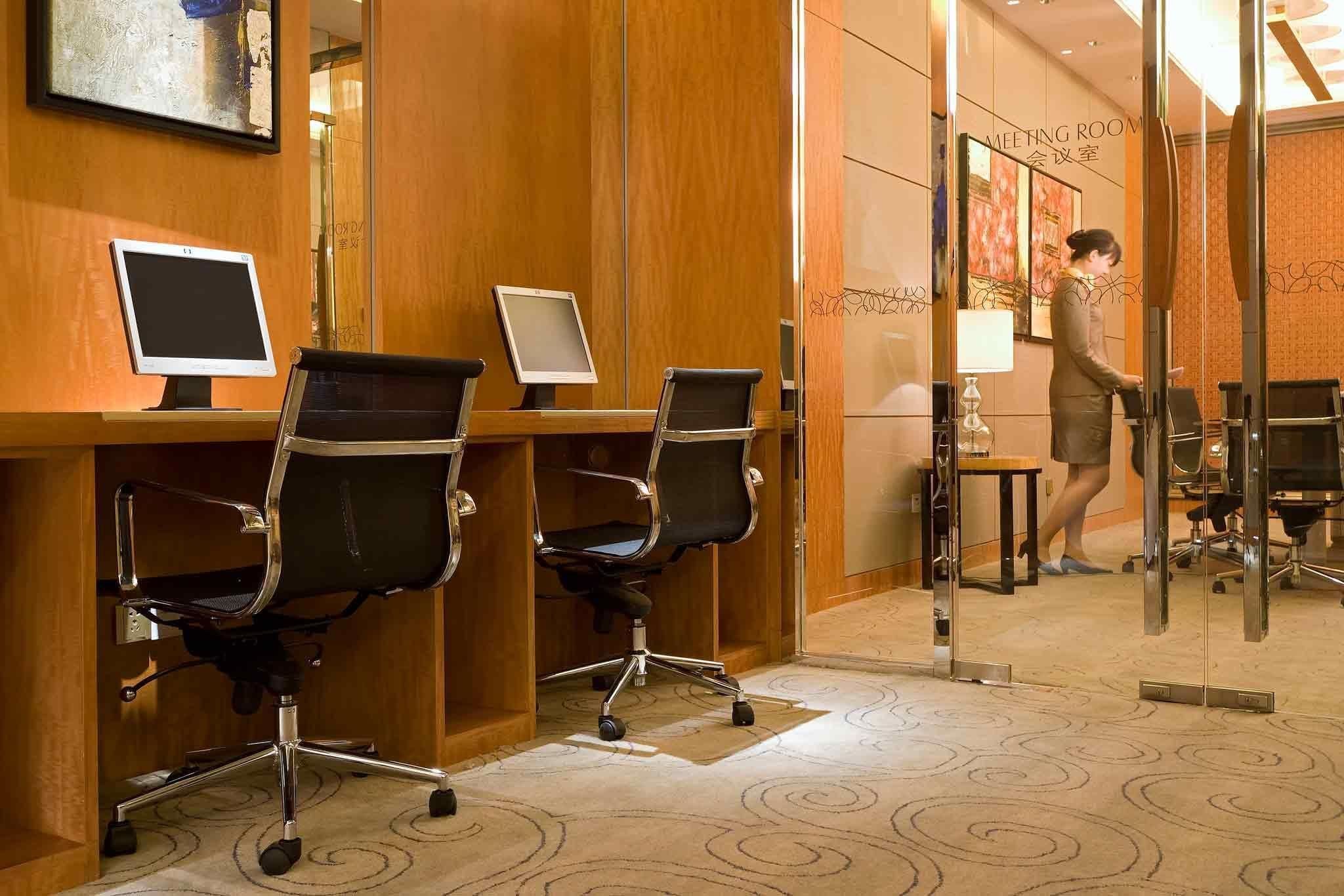 Un espace d’accueil d’hôtel avec un lambris en bois, deux écrans d’ordinateur, des chaises de bureau noires et une personne debout près d’une porte vitrée.