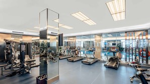 A modern gym with various exercise equipment, large windows, and a pool area visible through the glass.