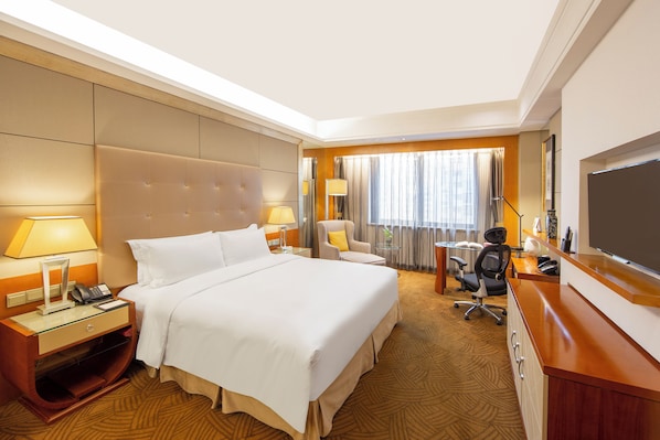 A hotel room with a large bed, bedside tables, a desk with a chair, a television, and a window with curtains.