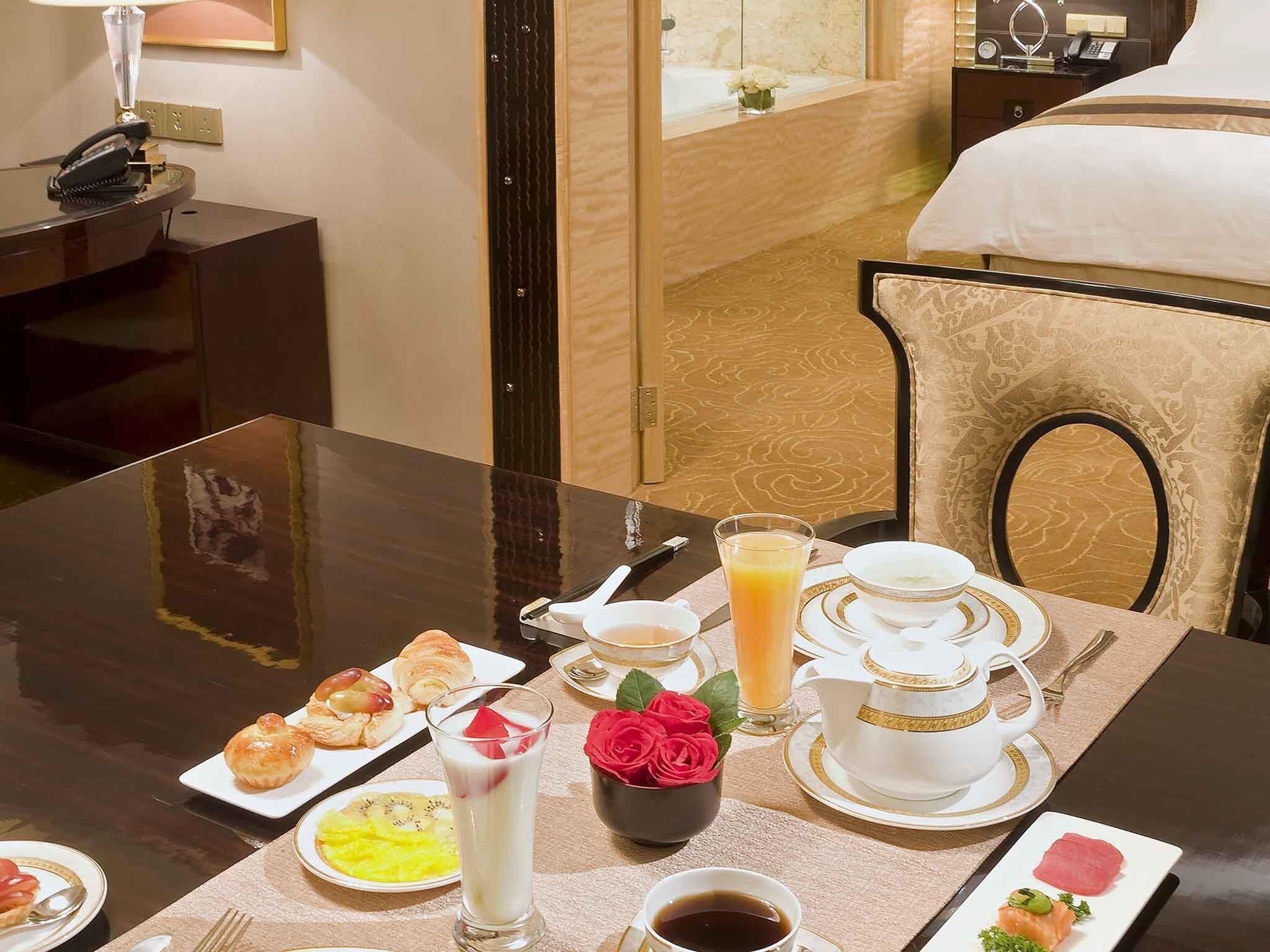 Habitación de hotel con una mesa de desayuno dispuesta, que incluye croissants, fruta, un vaso de jugo de naranja y una taza de café.