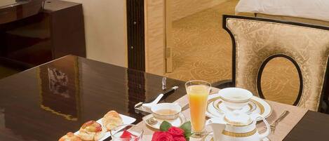 Habitación de hotel con una mesa de desayuno dispuesta, que incluye croissants, fruta, un vaso de jugo de naranja y una taza de café.