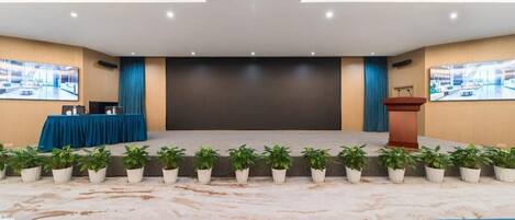 Un salón de conferencias con un escenario, un atril y una fila de plantas en macetas.