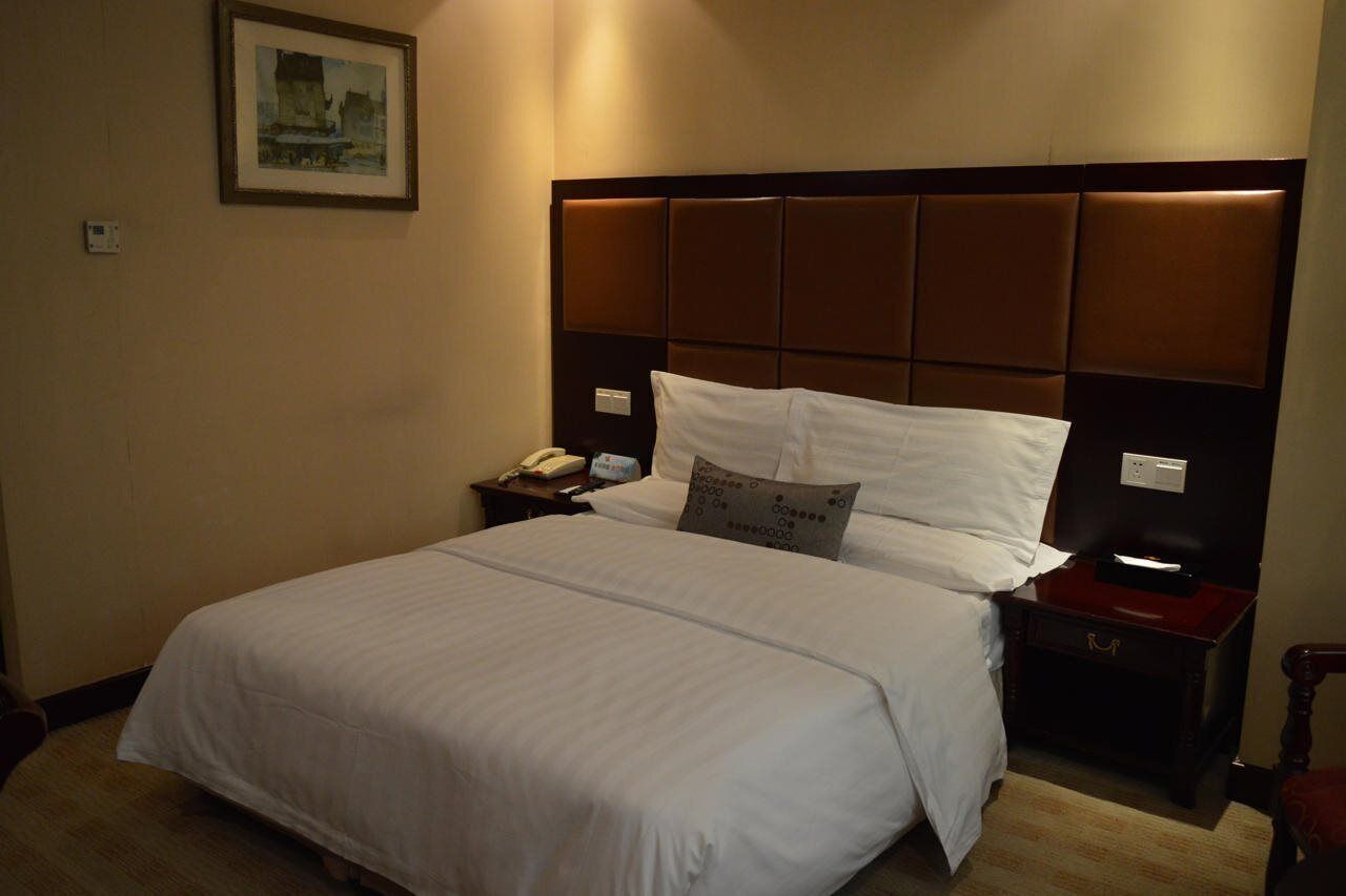 A hotel room with a large bed, a nightstand with a lamp, a telephone, and a framed picture on the wall.