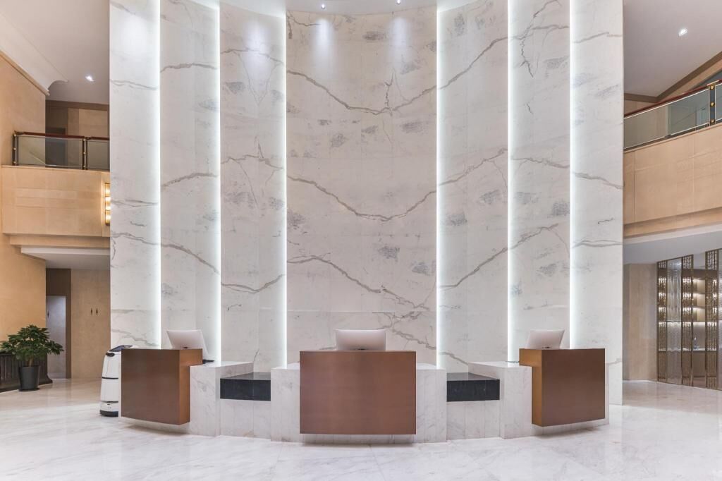 A modern lobby with marble columns, reception desks, and a high ceiling.