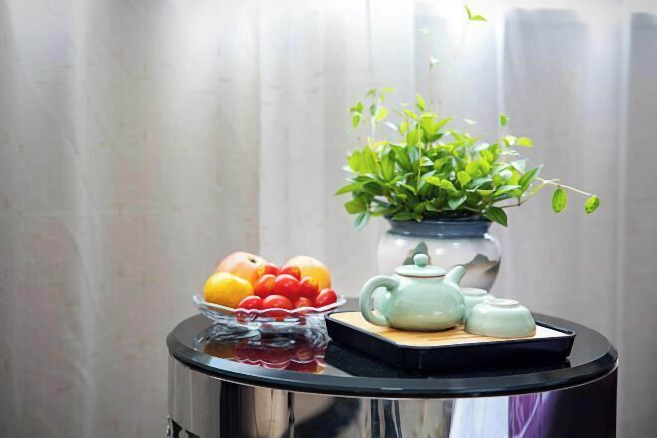 A table with a fruit bowl, a vase with green plants, and a teapot set.