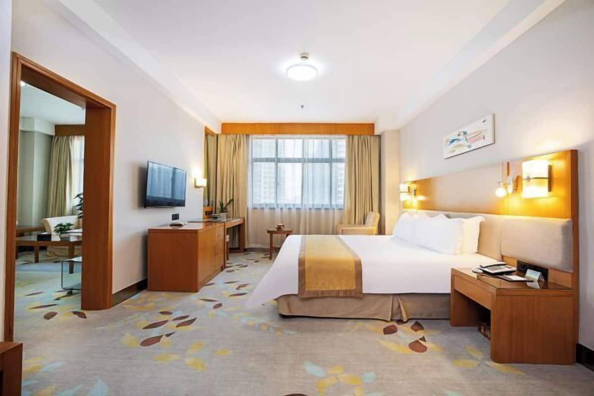 Habitación de hotel con cama, mesitas de noche, televisión, escritorio, silla y ventana con cortinas.