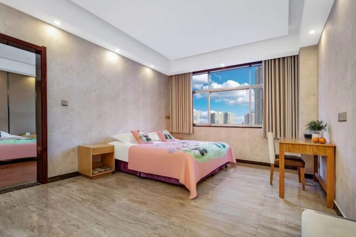 Un dormitorio con cama, mesita de noche, silla y ventana con vista a la ciudad.