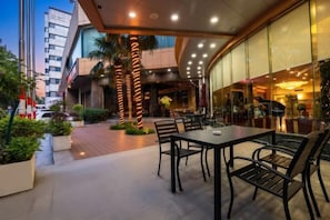 An outdoor dining area with tables and chairs, palm trees, and a building with large windows.
