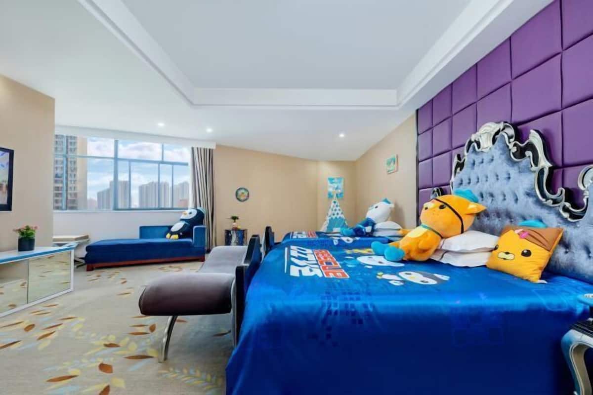 Habitación de hotel con una cama grande, una colcha azul, un cabecero morado y vistas a la ciudad.