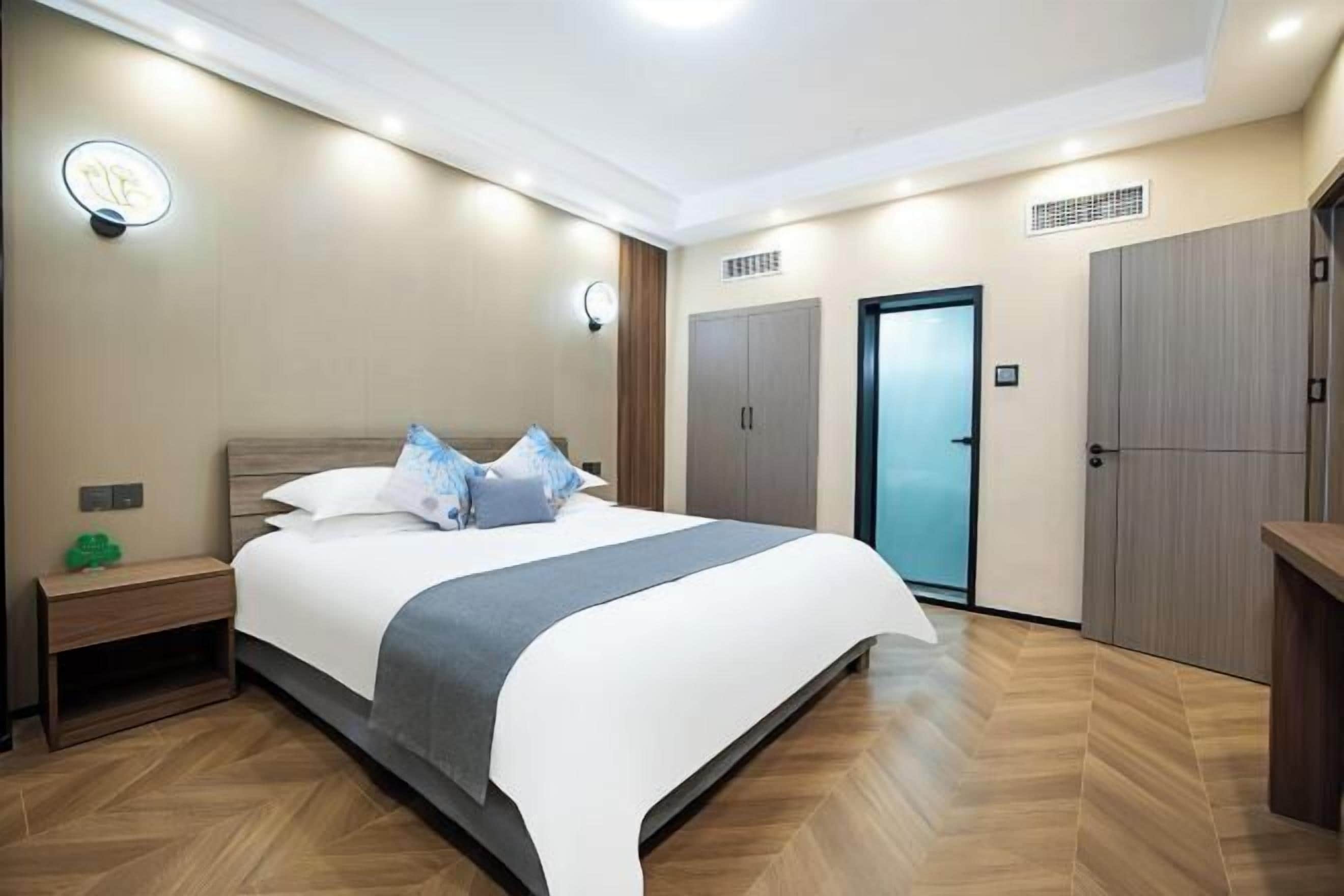 A modern hotel room with a large bed, bedside tables, a wardrobe, and a bathroom door.