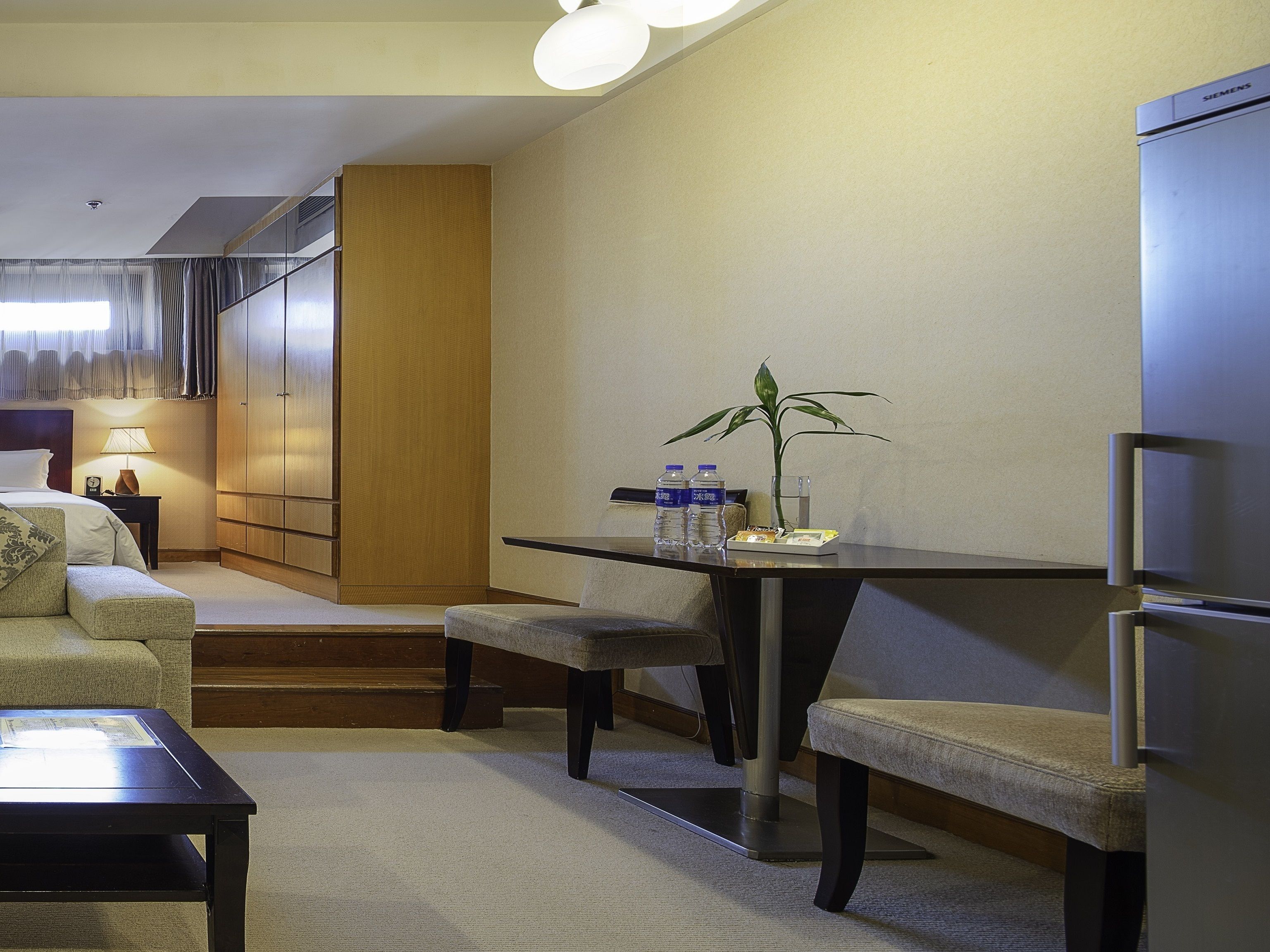 Ein Hotelzimmer mit Bett, Schreibtisch, Stuhl, Sofa, Esstisch, Kühlschrank und einer Topfpflanze.