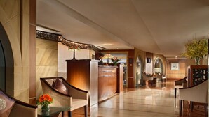 A hotel lobby with a reception desk, seating area, and a large vase with flowers. - Dalian Asia Pacific Service Apartment (Dalian)