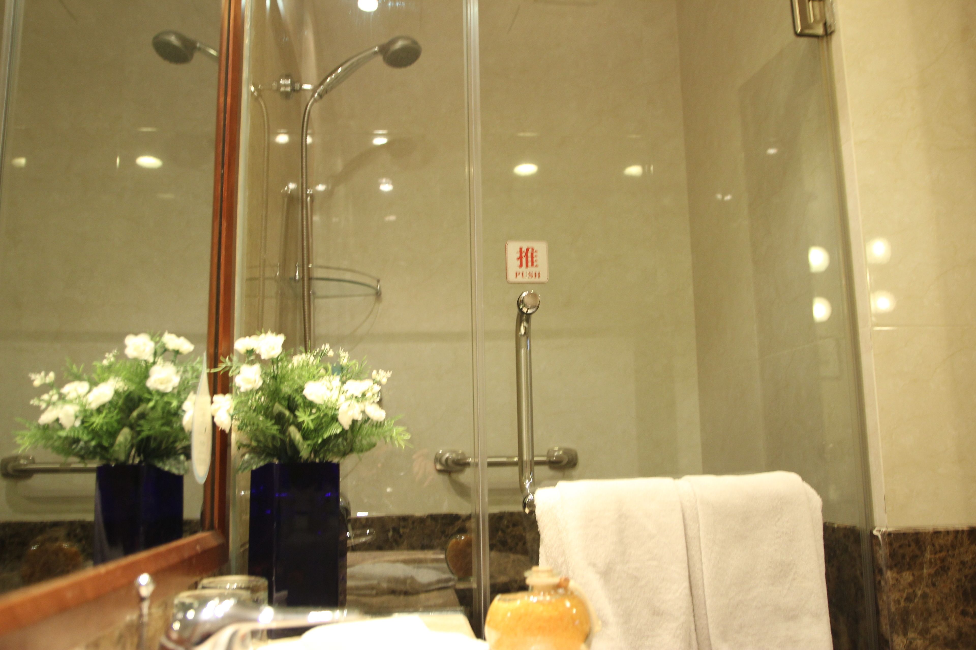 Un baño con cabina de ducha de vidrio, un perchero y un espejo con un florero.