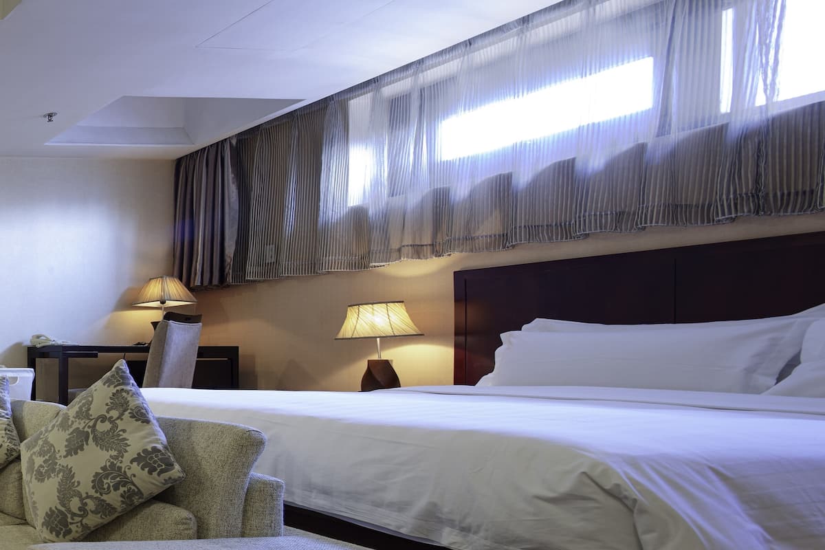 A hotel room with a large bed, a chair, two lamps, and a window with curtains.