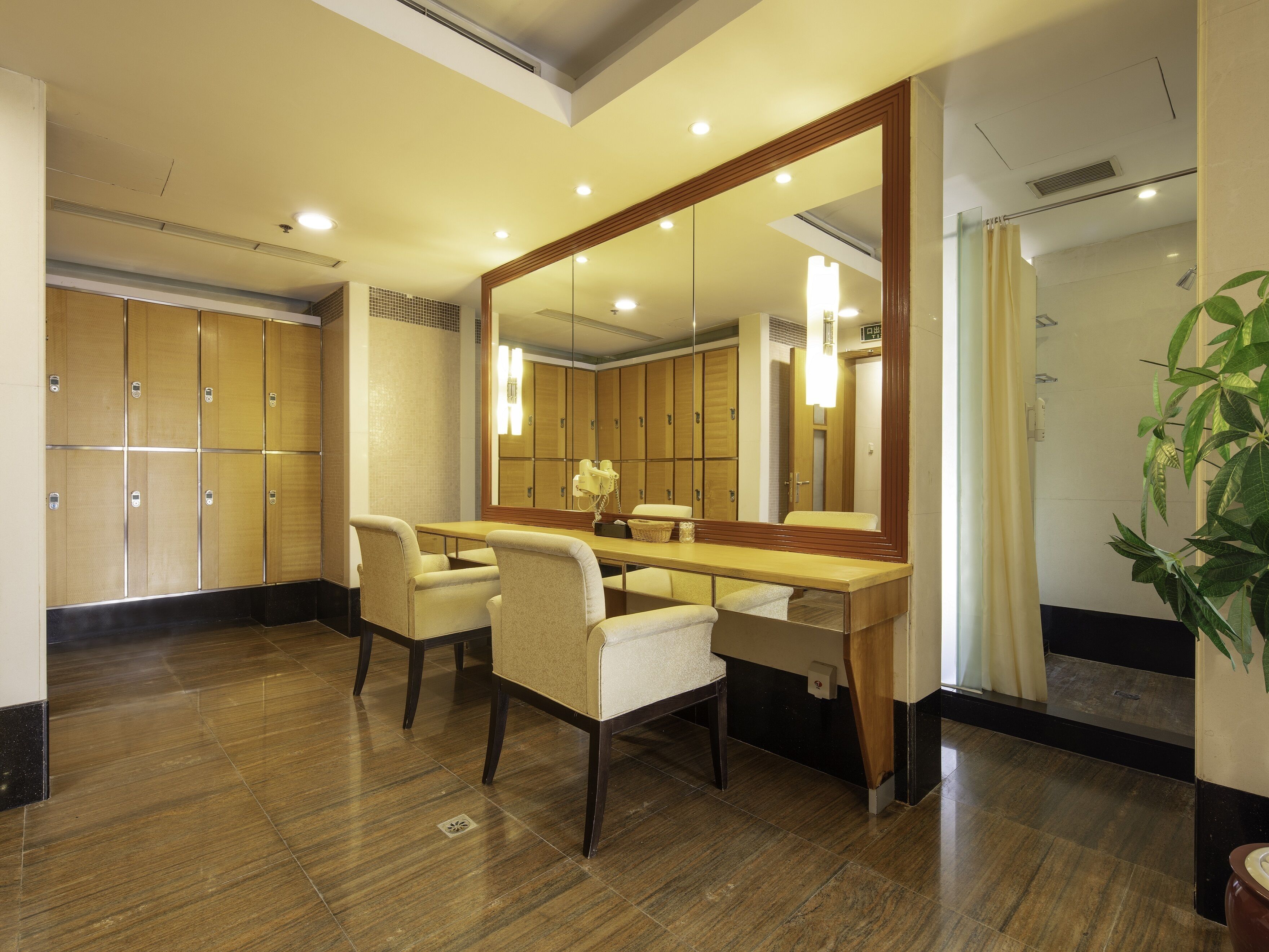 A hotel room with a wooden vanity, two chairs, a large mirror, and a potted plant.