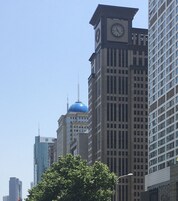 Un paisaje urbano con una imponente torre del reloj, un edificio con cúpula azul y modernos rascacielos.