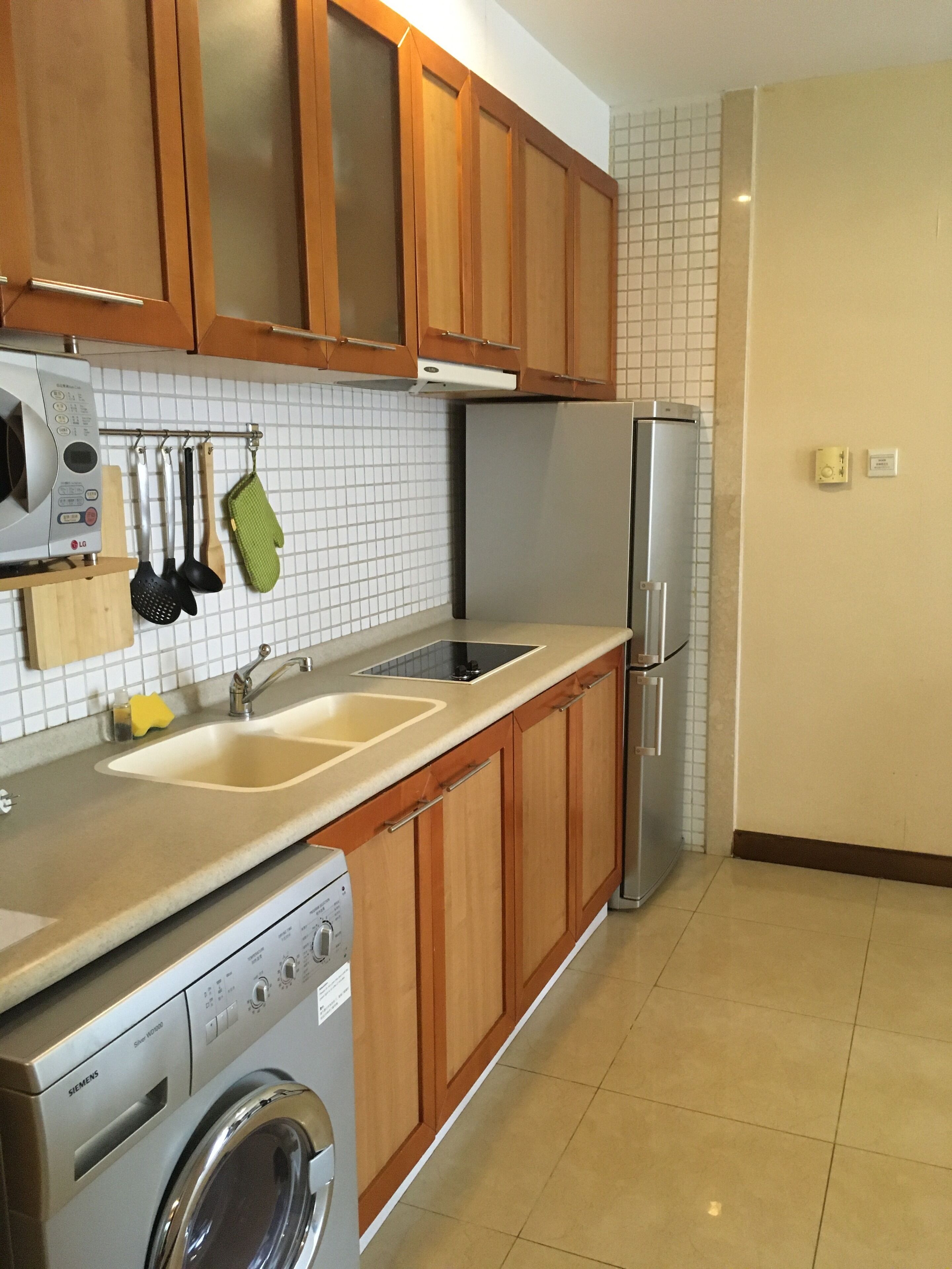 A kitchen with wooden cabinets, a stainless steel refrigerator, a washing machine, and a double sink.