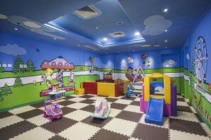 Un salón infantil con suelo a cuadros, estructuras de juego coloridas y murales en las paredes.