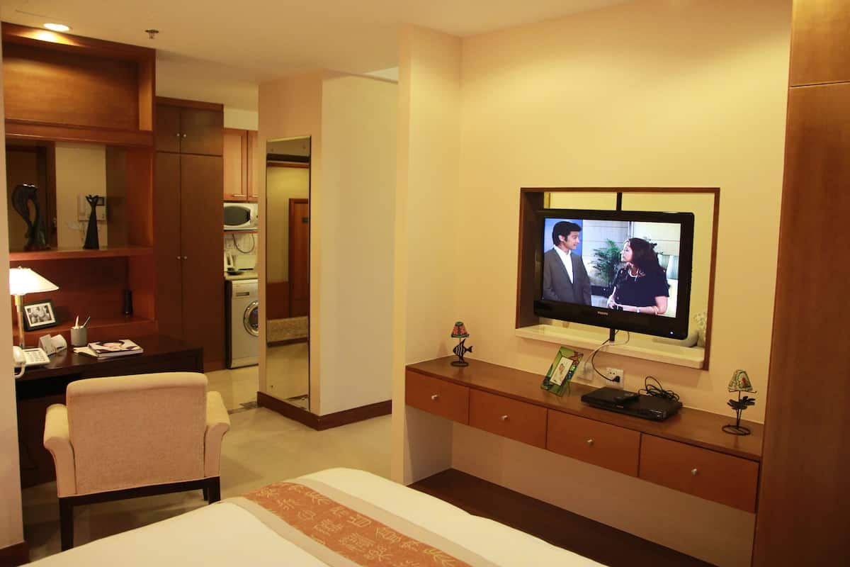A hotel room with a bed, a desk with a lamp, a television mounted on the wall, and a small cabinet.