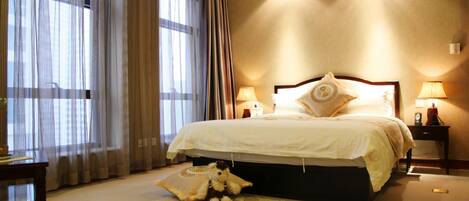 A hotel room with a large bed, two bedside lamps, a small table, and a teddy bear on a rug.