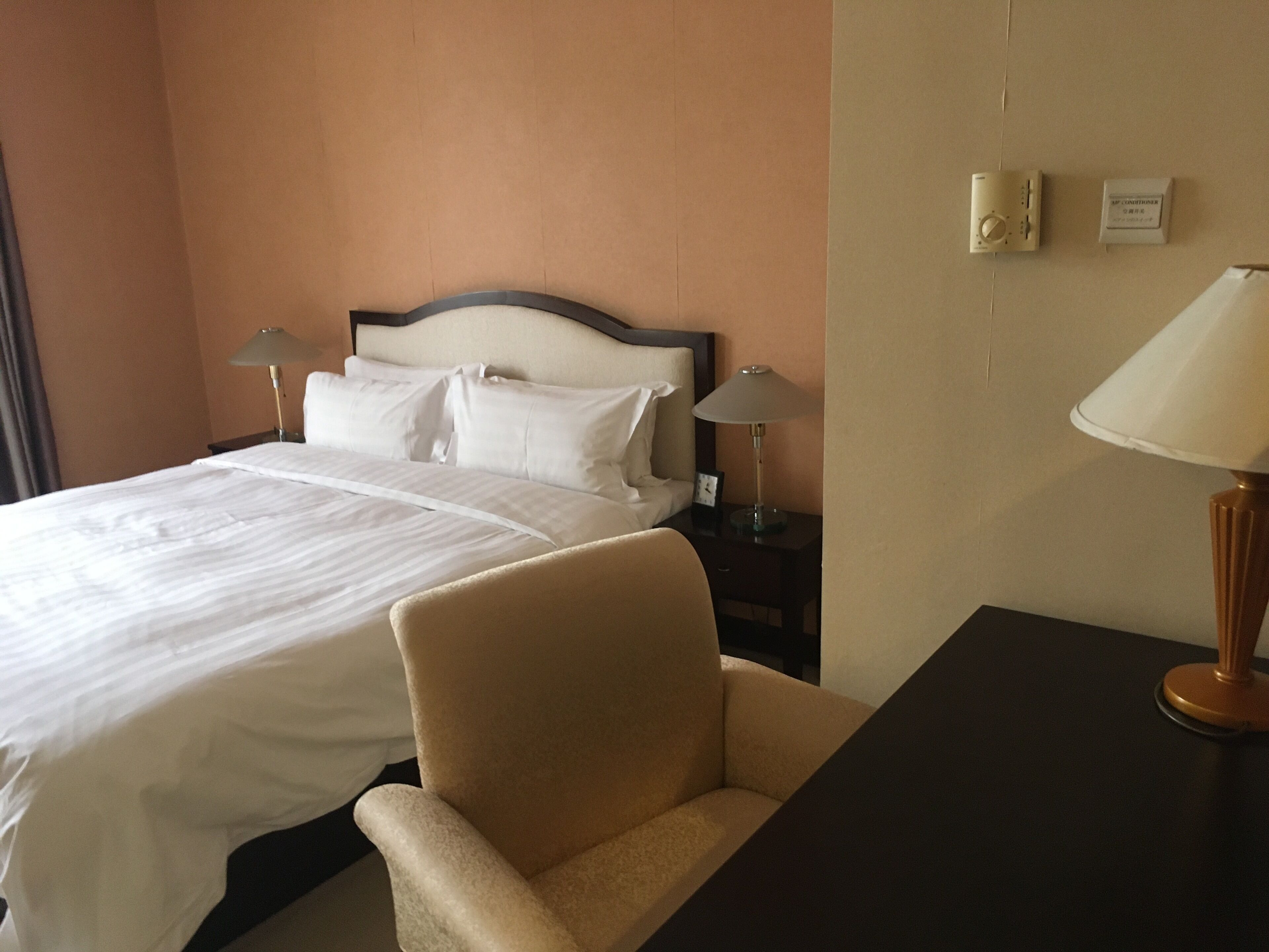A hotel room with a bed, two bedside lamps, a nightstand, a chair, and a desk.