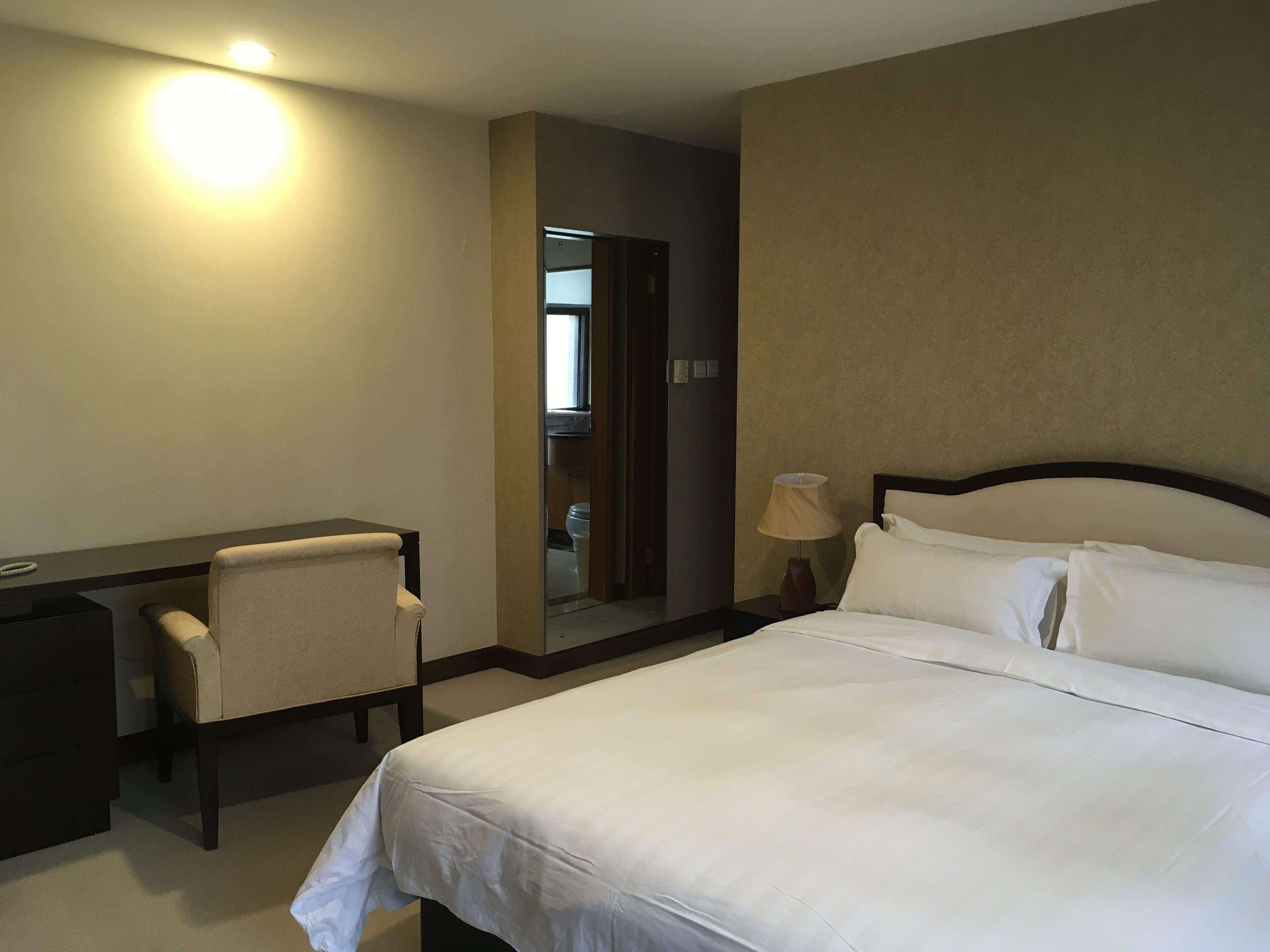 A hotel room with a bed, a desk, a chair, a lamp, and a mirror.