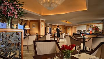 A hotel dining area with tables set for guests, a bar area, and a service staff member.