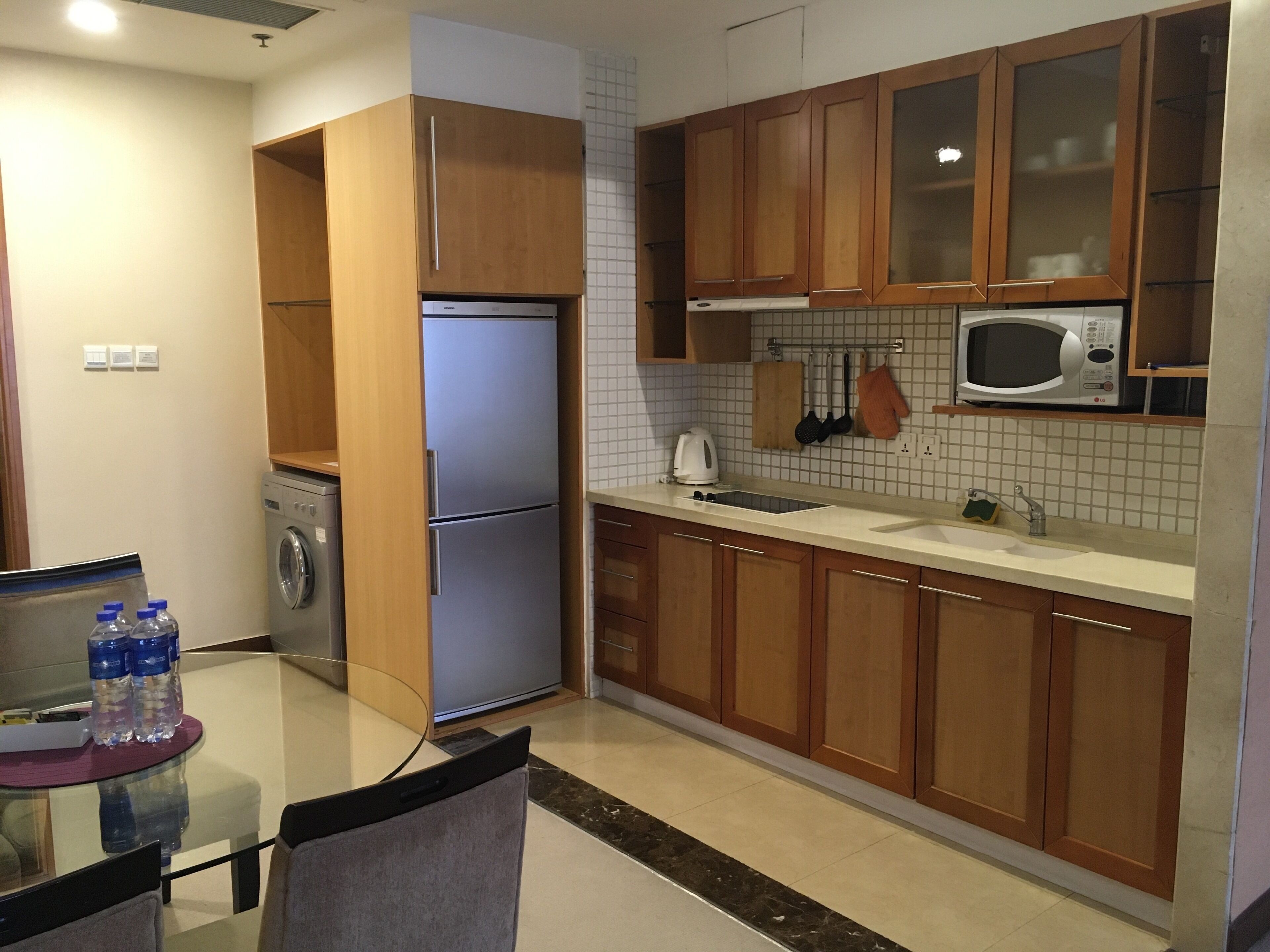 Una cucina compatta con mobili in legno, un frigorifero in acciaio inossidabile, un forno a microonde e una lavatrice.