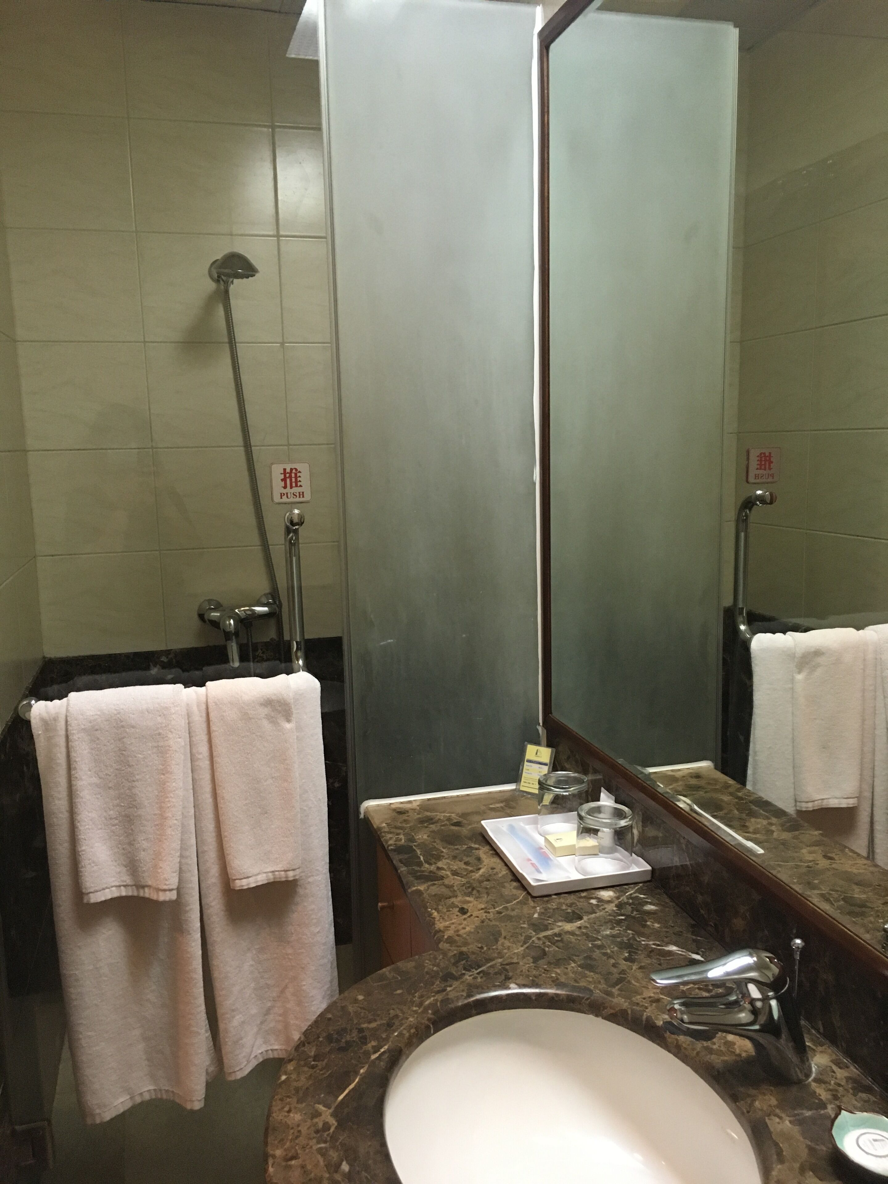 Un baño con lavamanos, espejo, toallero y ducha.