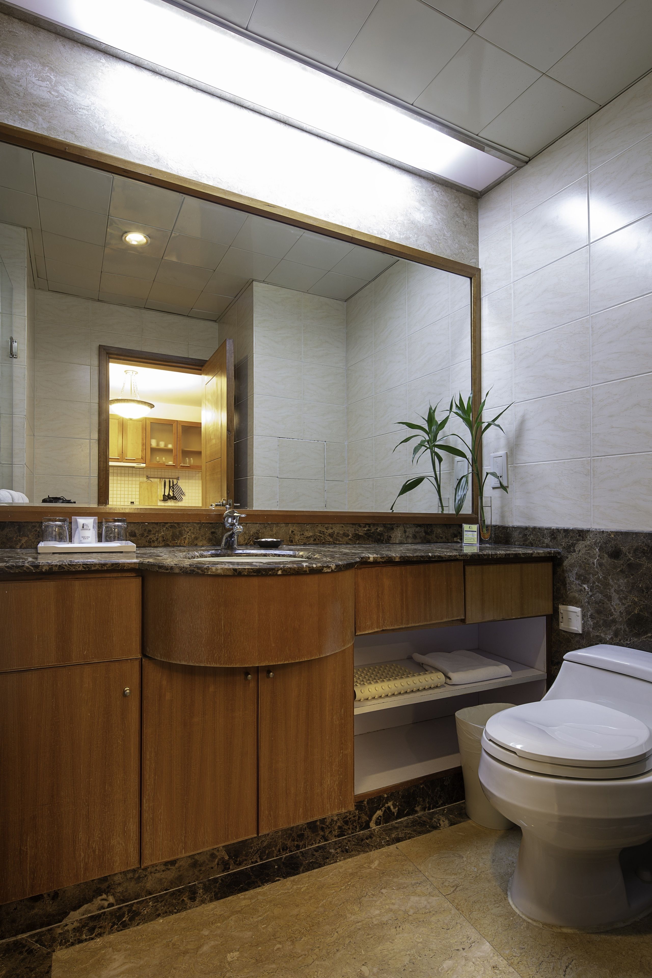 A modern bathroom with a wooden vanity, a large mirror, a toilet, and a sink.