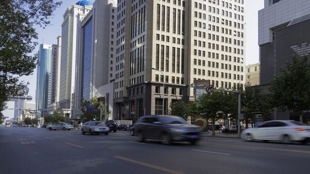 A tall building with a clock tower, surrounded by other high-rise buildings and a busy street with cars. - Dalian Asia Pacific Service Apartment (Dalian)