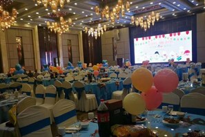 A banquet hall with round tables, chairs, and a stage with a screen.