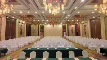 A banquet hall with rows of white chairs, tables with green tablecloths, and a chandelier.