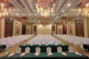 Une salle de banquet avec des rangées de chaises blanches, des tables recouvertes de nappes vertes et un lustre.