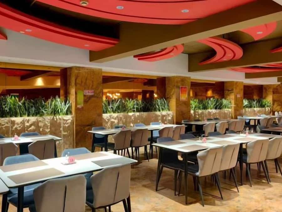 Un restaurant doté de nombreuses tables et chaises, d’un mur en pierre agrémenté de plantes et d’un plafond rouge au design original.