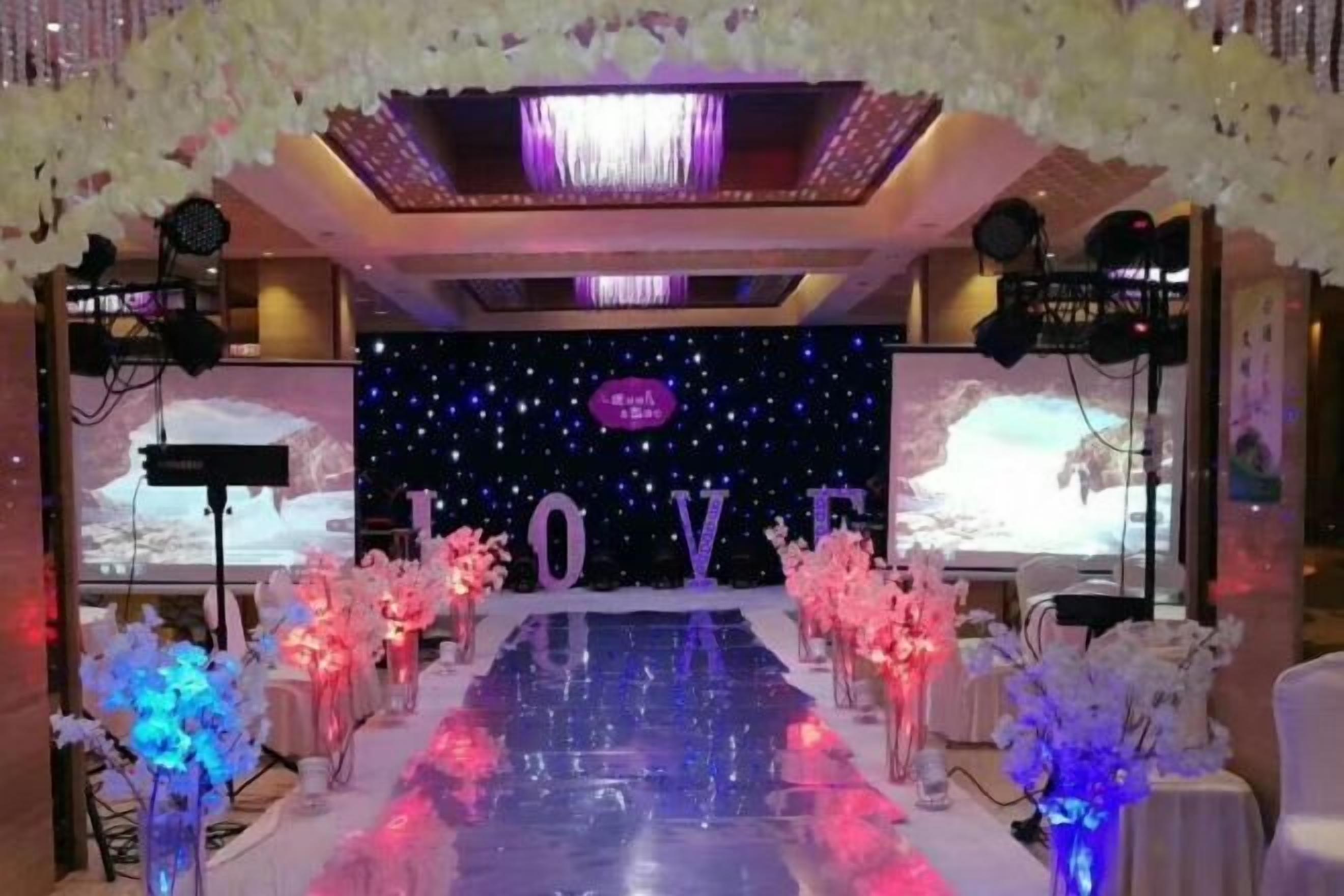A stage with a 'LOVE' backdrop, surrounded by floral arrangements and a reflective floor.
